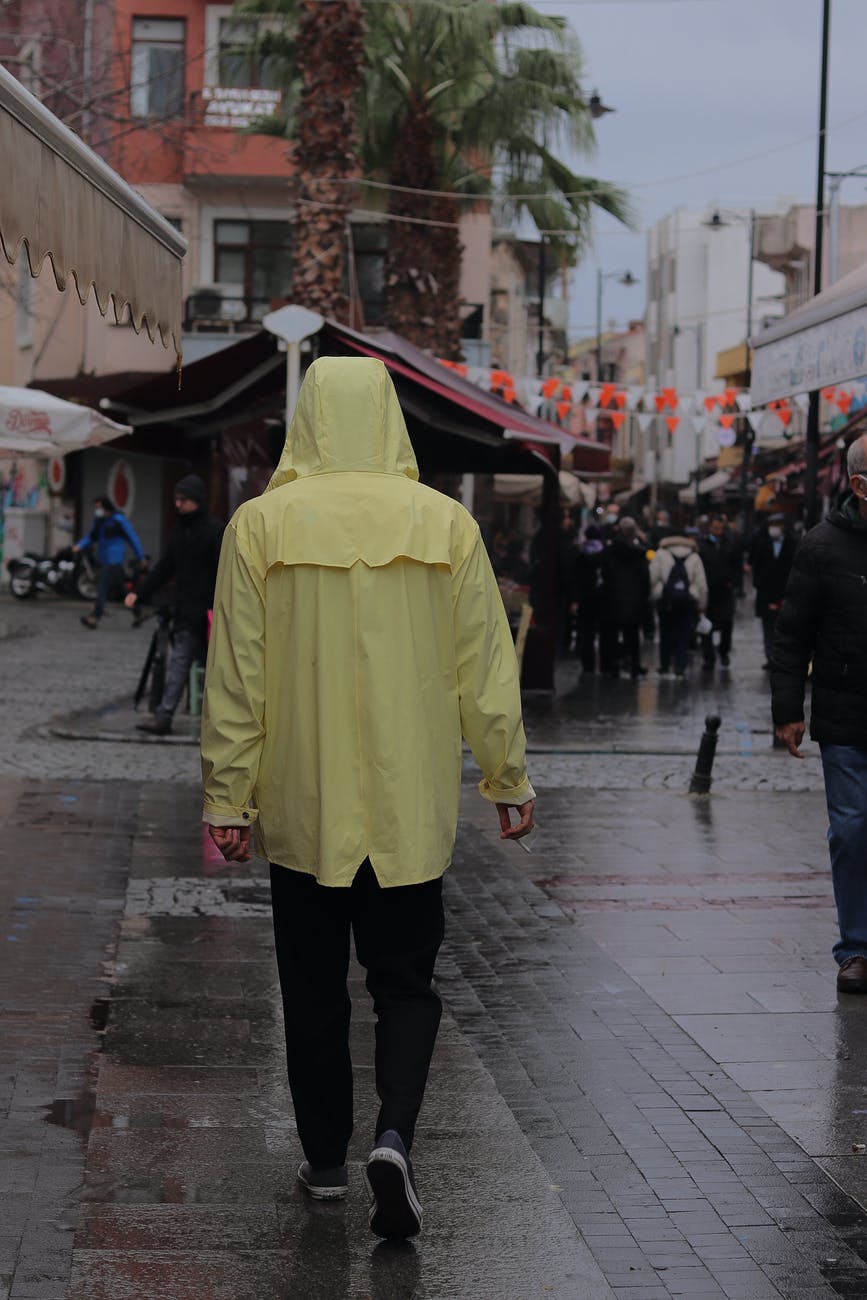 a person in yellow hoodie jacket walking on a wet sidewalk